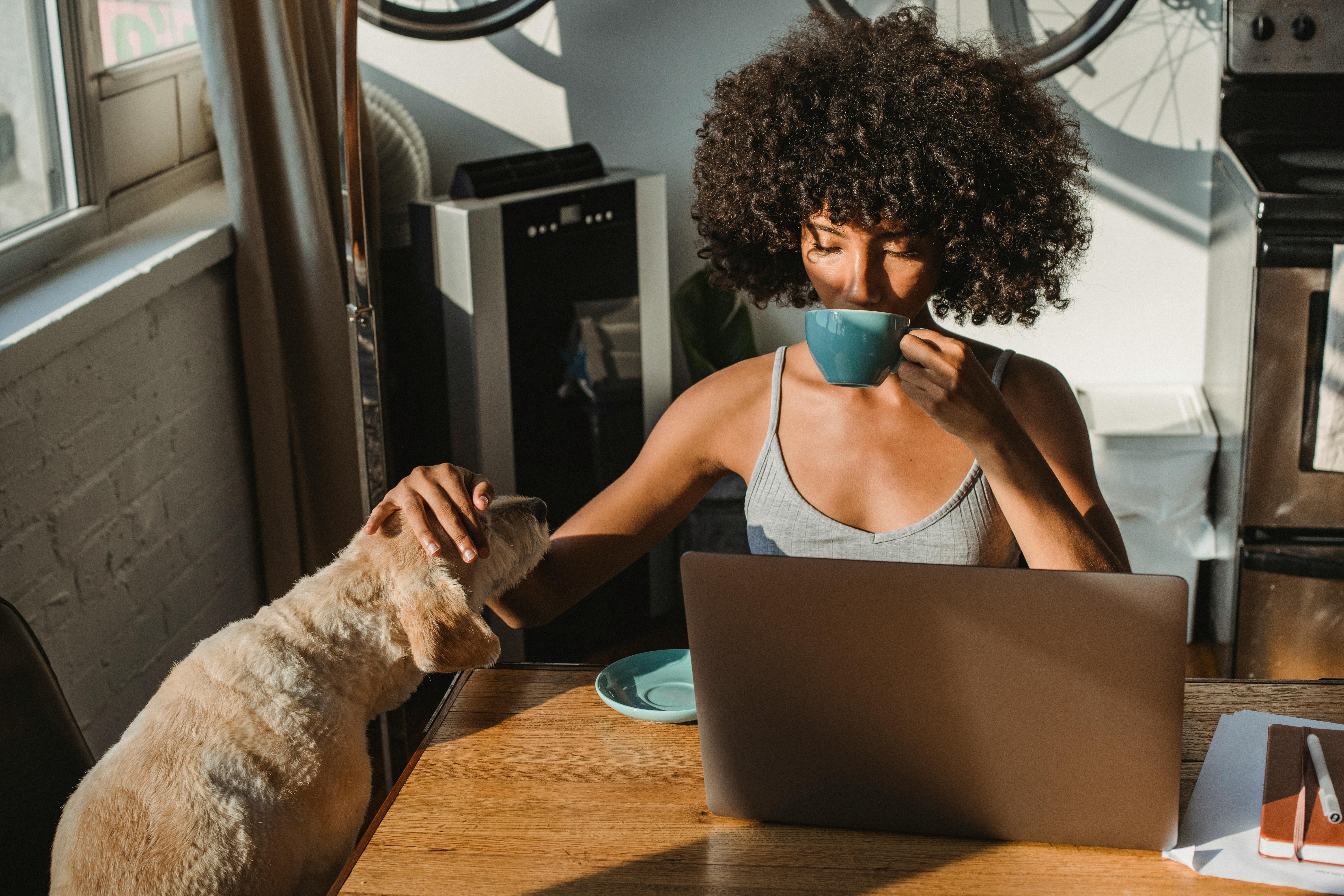 Person drinking out of a mug while petting a dog